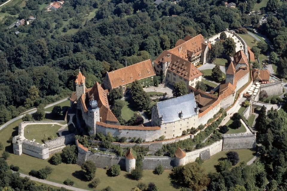 An aerial view of a historic castle complex surrounded by dense forest.