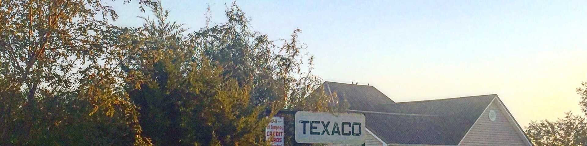 Paisagem rural com uma casa identificada como 'TEXACO' e um caminhão antigo. Há placas indicando 'CARTÕES DE CRÉDITO' e 'WALTERS WORKS'.