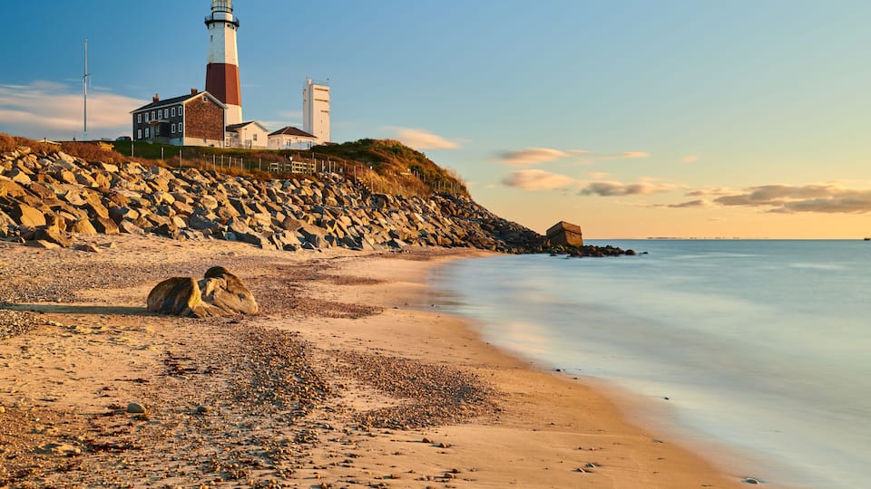 A coastal landscape with a lighthouse, rocky beach, and calm sea.