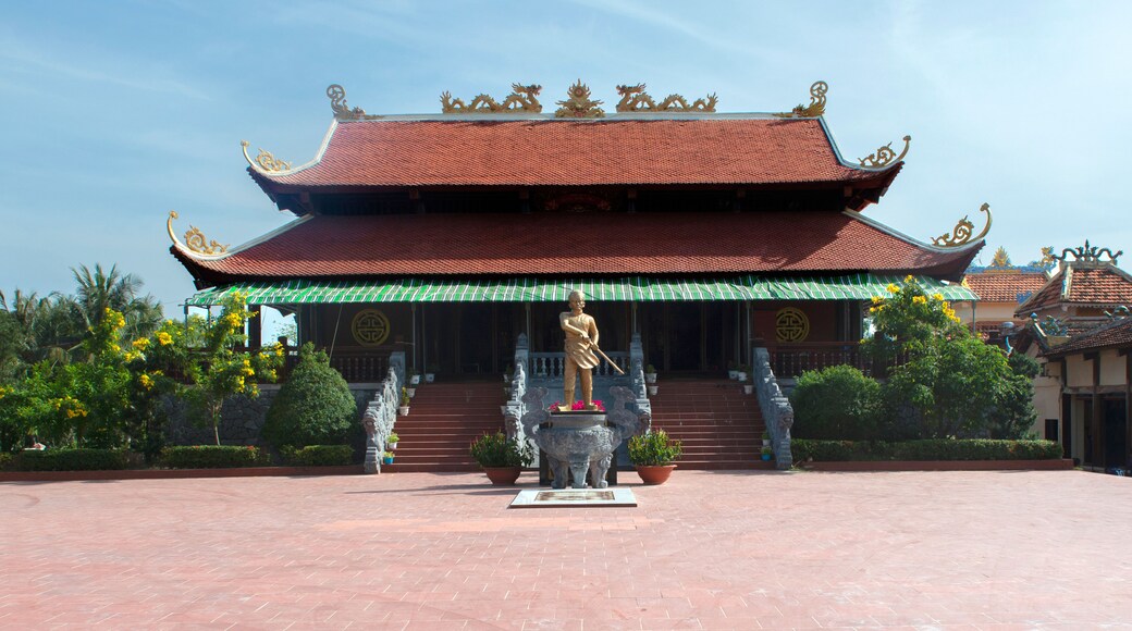A traditional temple with a red tiled roof, ornate golden decorations, and a statue in front.