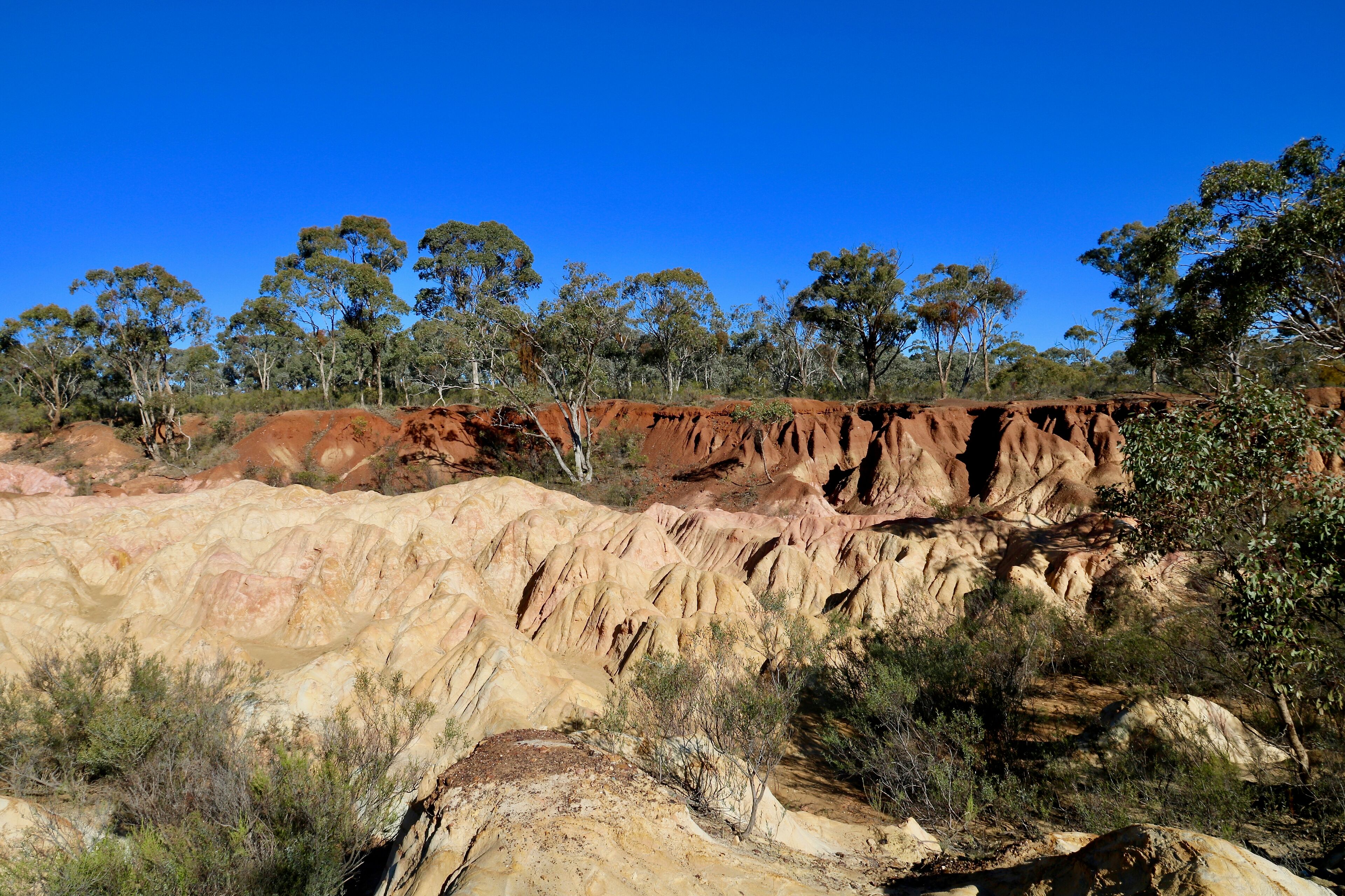 A rugged landscape with reddish-brown rock formations and sparse vegetation under a clear blue sky.
