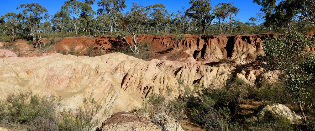 A rugged landscape with reddish-brown rock formations and sparse vegetation under a clear blue sky.