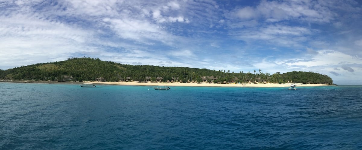 A tropical island with a beach, clear turquoise waters, and a small boat.