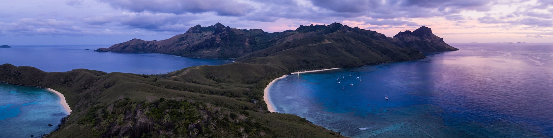 A coastal landscape with mountains, a beach, and clear blue waters.