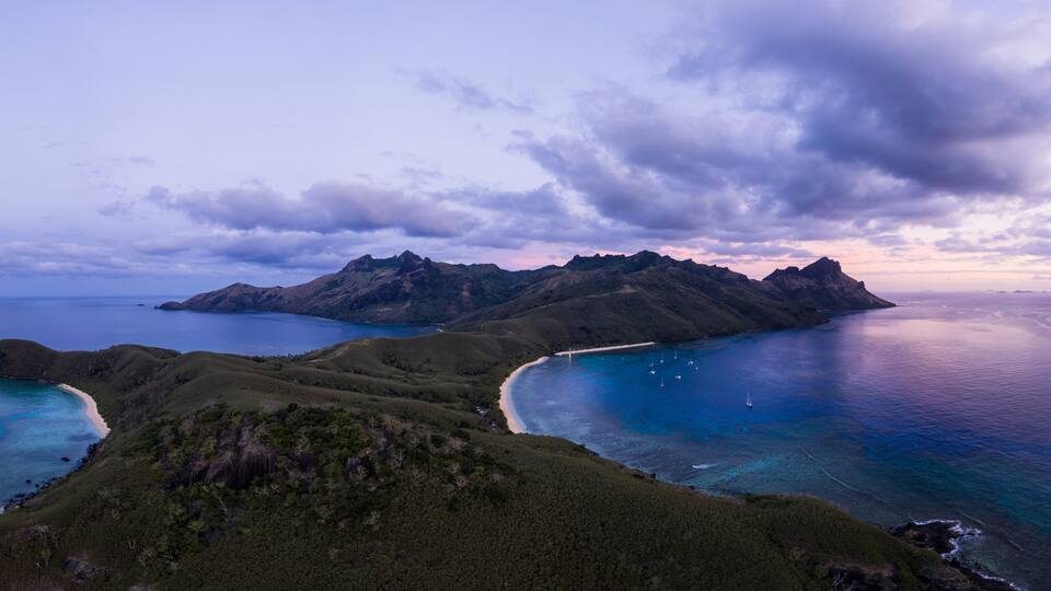 A coastal landscape with mountains, a beach, and clear blue waters.