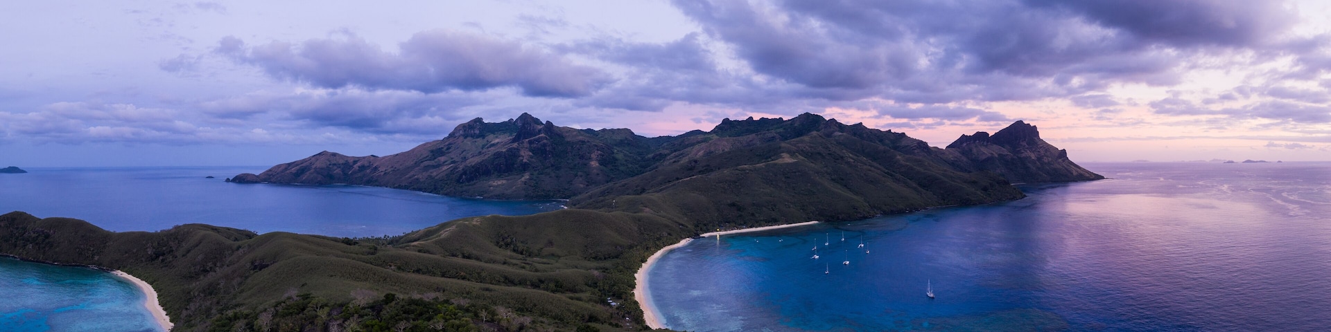Un paisaje costero con montañas, una playa y aguas azules cristalinas.