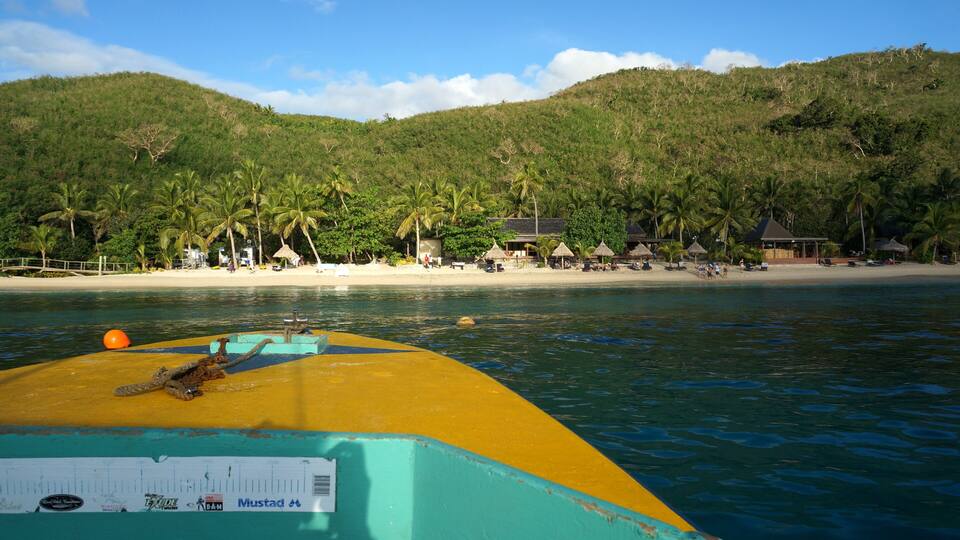 A boat on turquoise water with a beach and palm trees in the background.