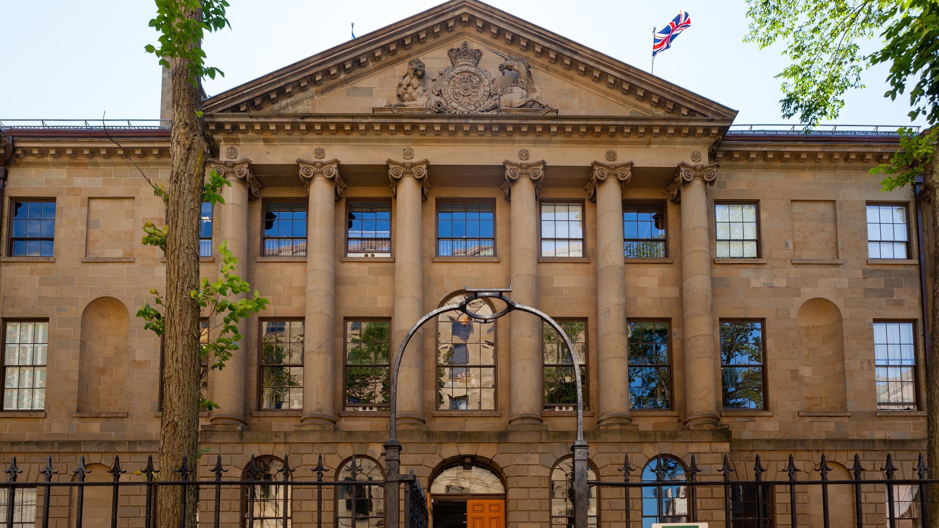 Un gran edificio de piedra con columnas, un escudo y una bandera.