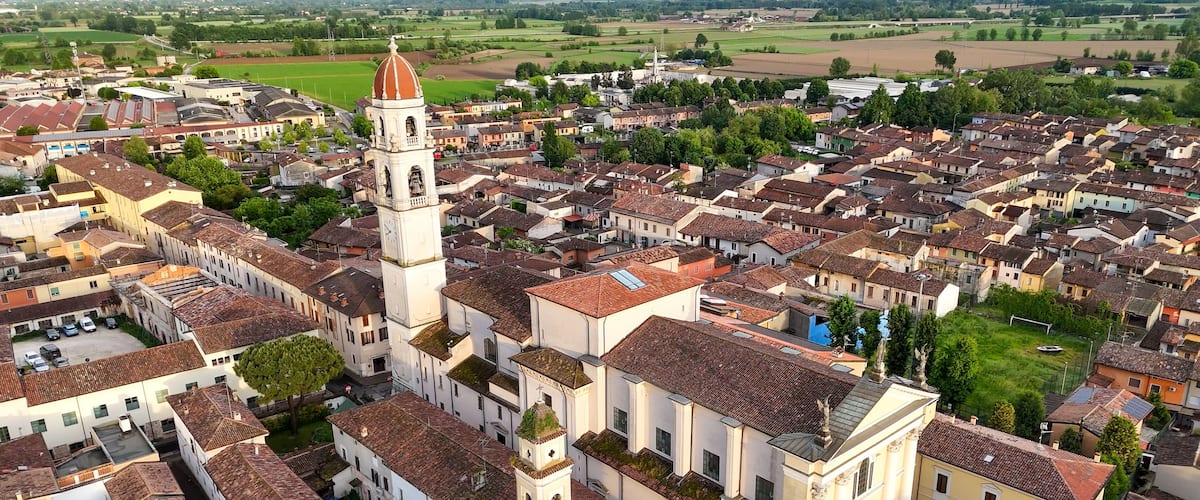 A town with a prominent church featuring a tall bell tower and a large dome, surrounded by closely packed buildings with red-tiled roofs.