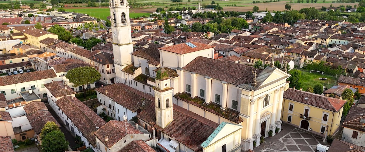 A historic town with a prominent church featuring a tall bell tower, surrounded by traditional buildings with red-tiled roofs.