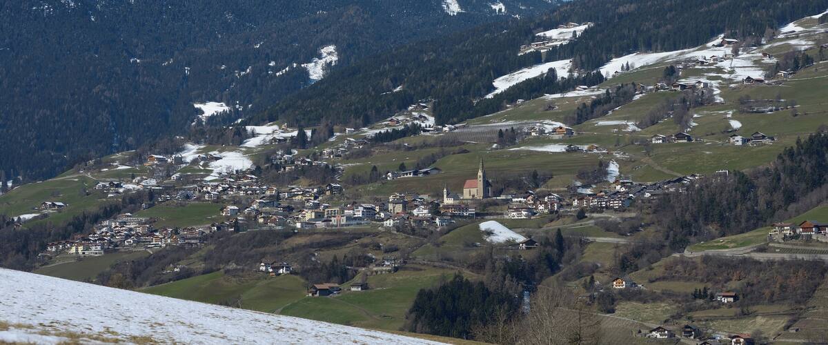 A mountainous village with snow patches, a church, and scattered houses.
