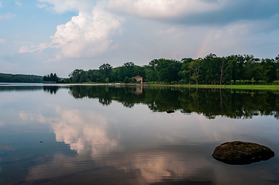 A calm lake with a reflection of trees and a rainbow.