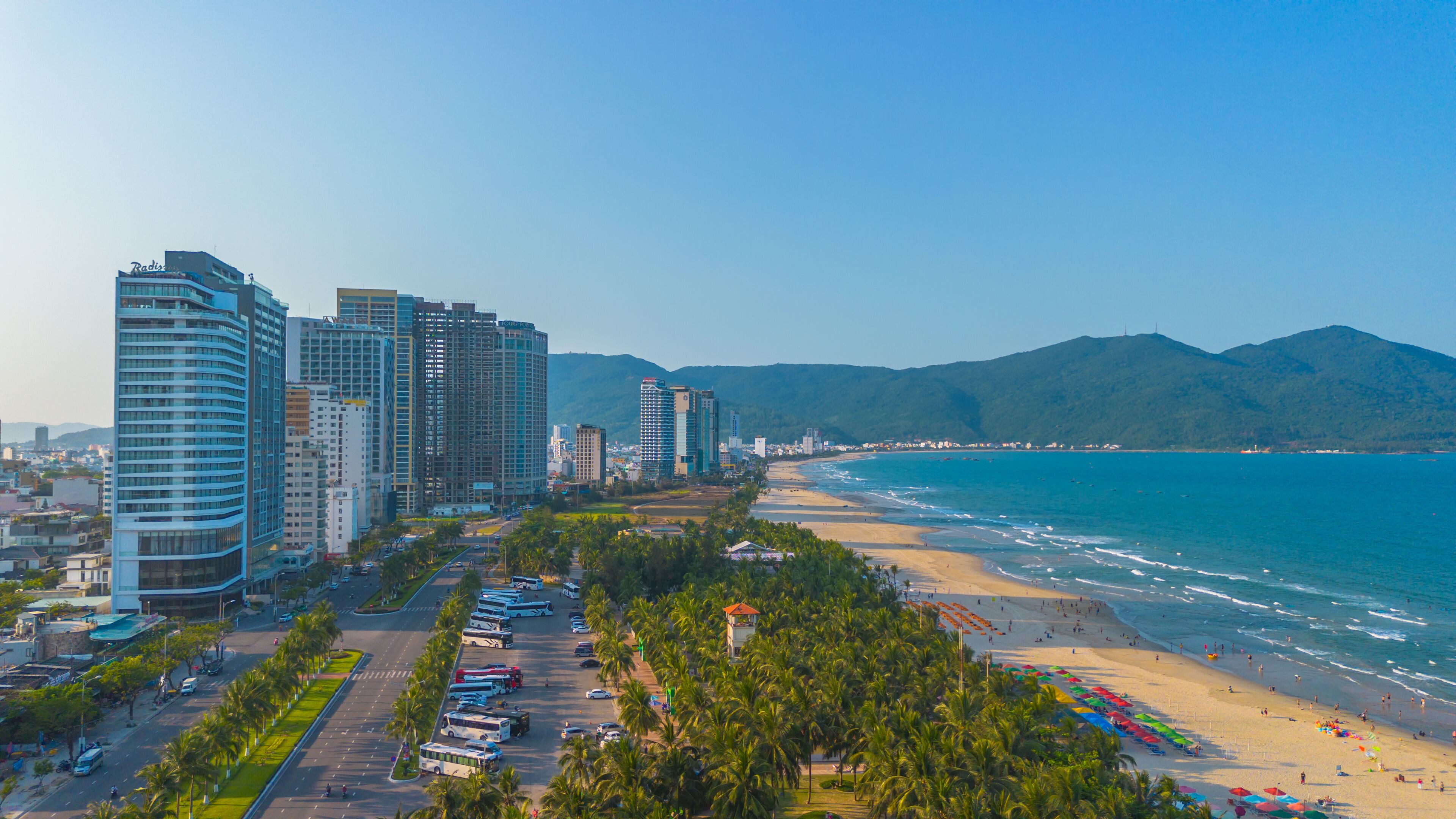 A coastal cityscape with high-rise buildings, a beach, and palm trees.