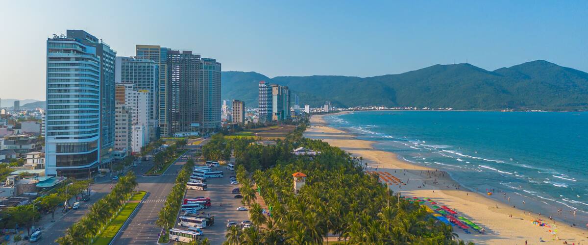 A coastal cityscape with high-rise buildings, a beach, and palm trees.