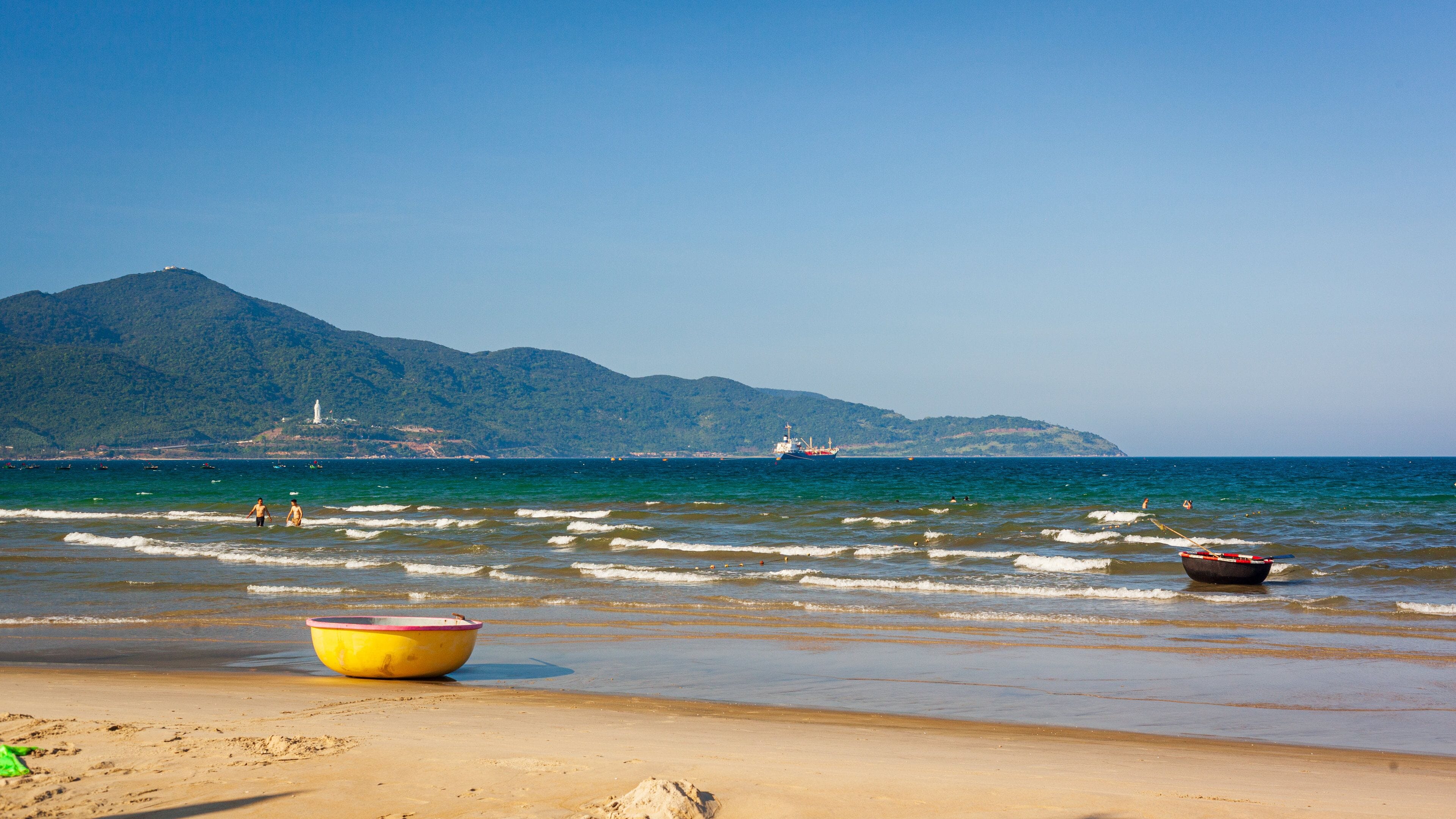 Ein Strand mit einem gelben Boot, einem kleinen Boot und einem Schiff in der Ferne.