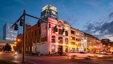 A city street at dusk with a historic building, a modern skyscraper, and a busy intersection.