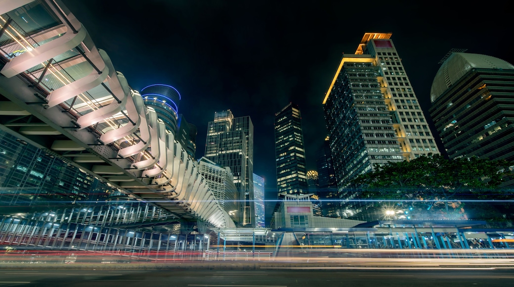 Paesaggio urbano notturno con architettura moderna, tra cui un edificio curvo con facciata in vetro e un grattacielo con finestre illuminate.
