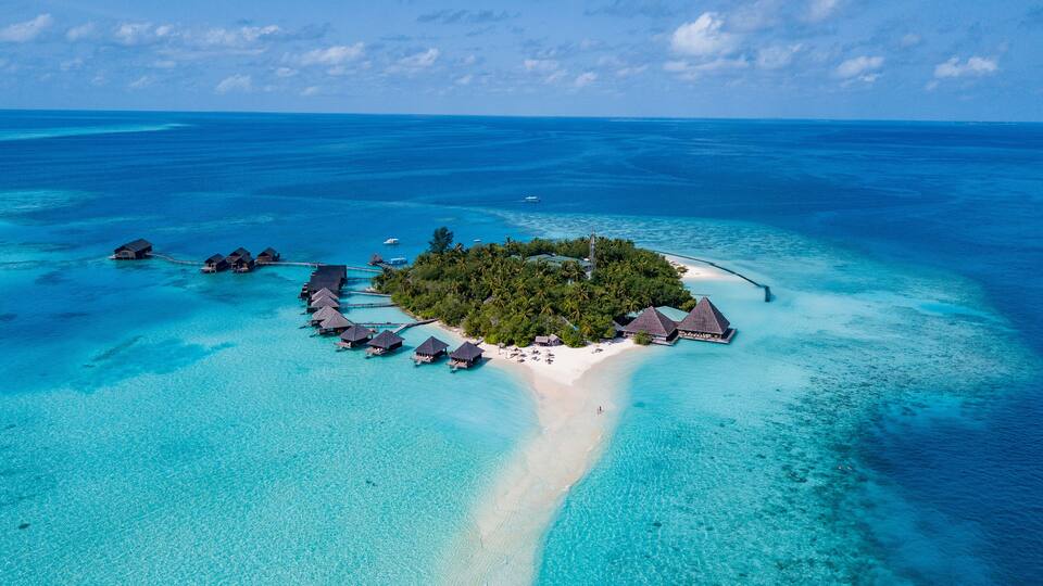 An aerial view of a tropical island with overwater bungalows, clear turquoise waters, and a sandy beach.