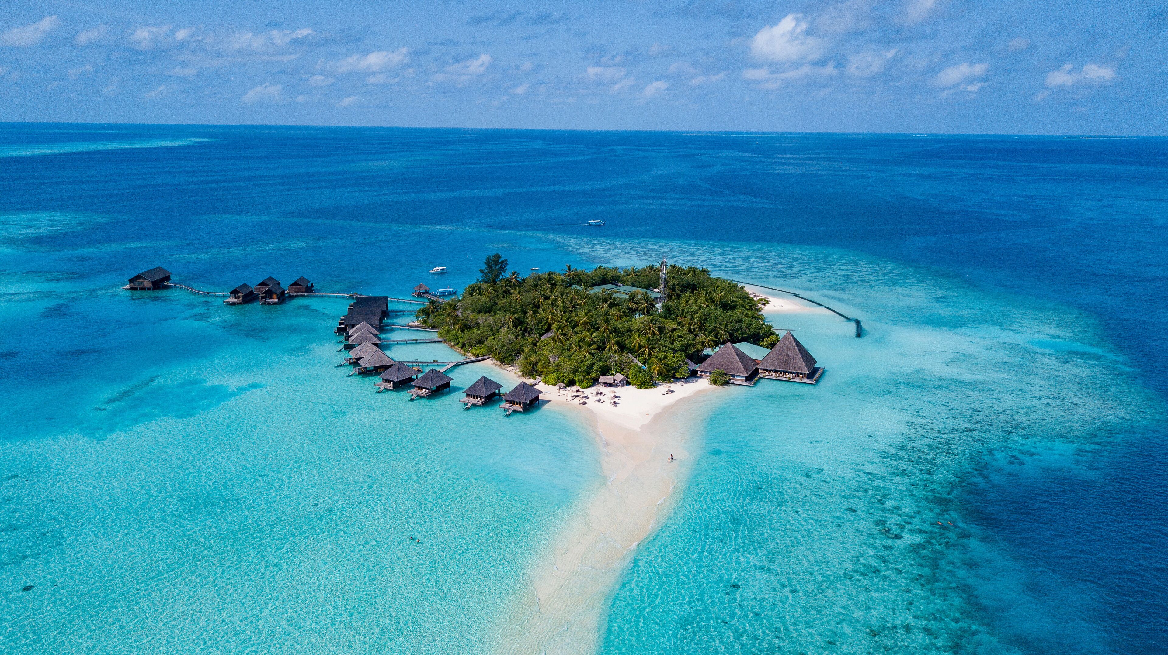 An aerial view of a tropical island with overwater bungalows, clear turquoise waters, and a sandy beach.