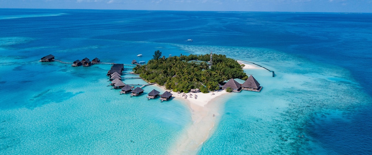 An aerial view of a tropical island with overwater bungalows, clear turquoise waters, and a sandy beach.