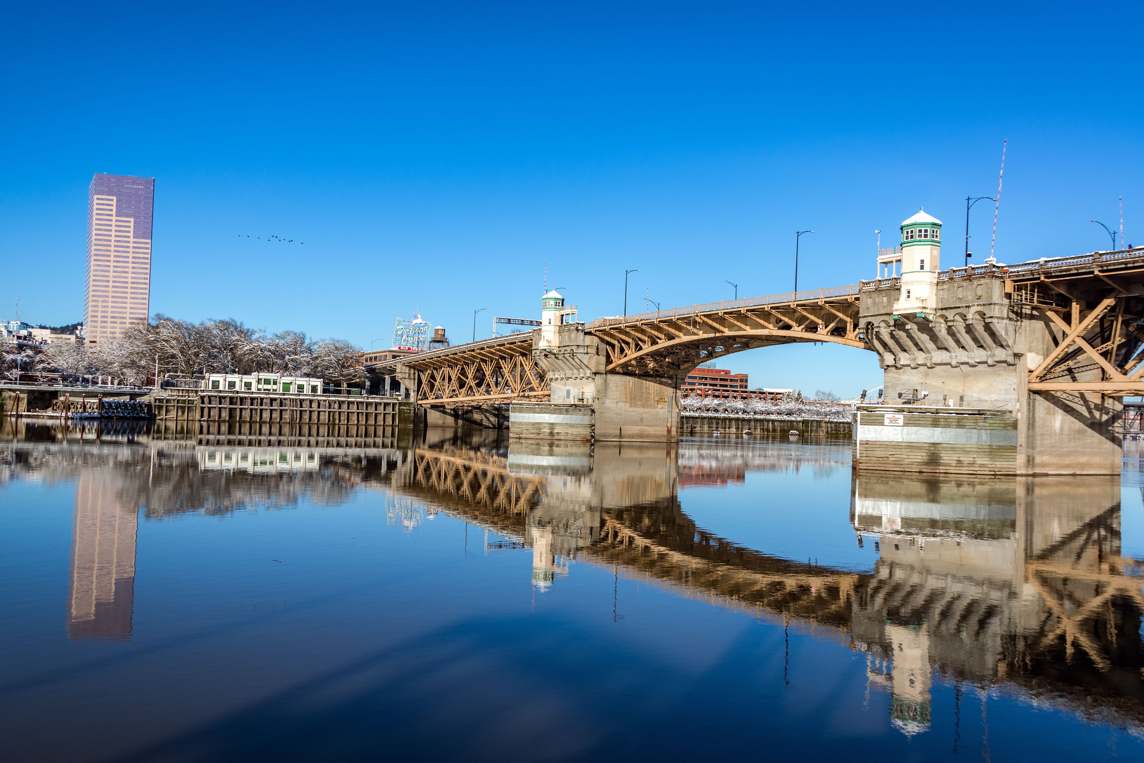 A bridge over a calm river with a clear reflection, a tall building, and a lighthouse.