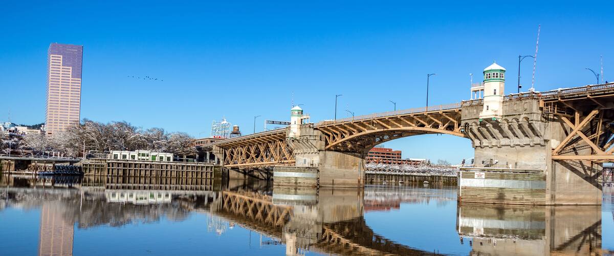 A bridge over a calm river with a clear reflection, a tall building, and a lighthouse.
