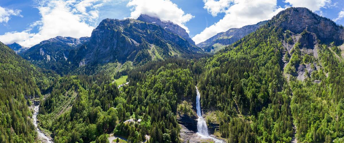 A mountainous landscape with a waterfall and dense forest.