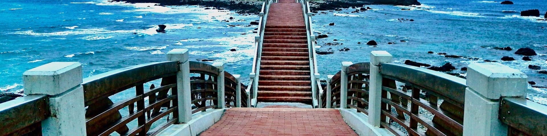 A coastal walkway leading to a rocky island with a bridge.