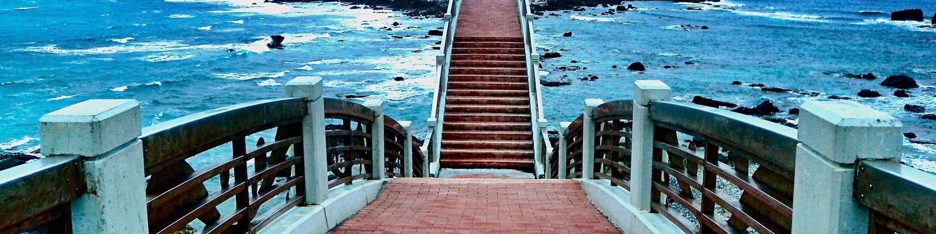 Un paseo marítimo que conduce a una isla rocosa con un puente.