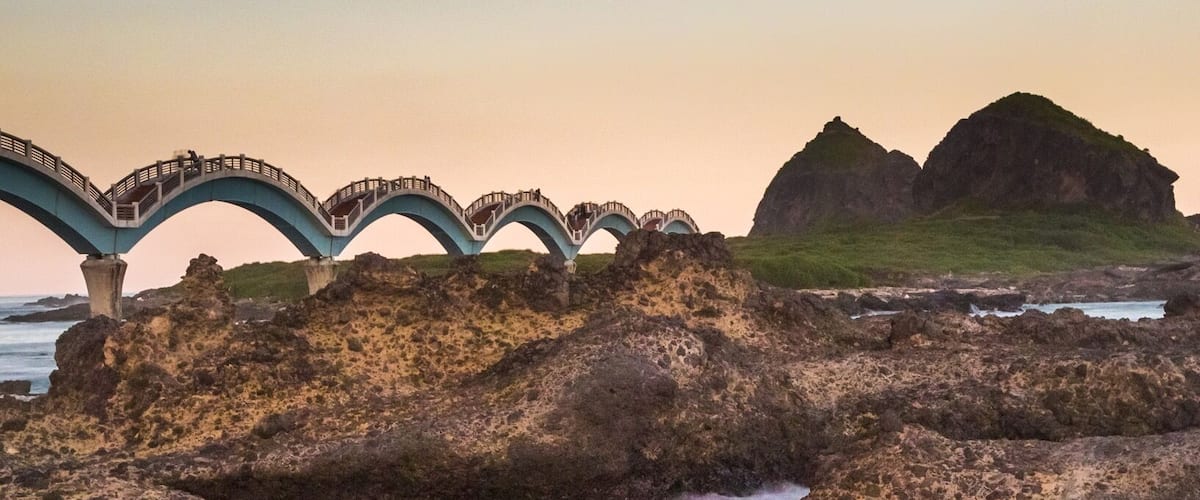 Spectacular volcanic landscape and tidal pools during dusk at Sanxiantal, Taiwan, along with the pedestrian Dragon Bridge. Captured during a stop along a coastal biking tour around the island over 10 days. Sanxiantal is on the SE edge and is also subject to spectacular sunrises. The bridge allows exploration of the outer island, “the platform if the three immortals”, and a much longer walking path allows exploration of the greater vicinity and shoreline.