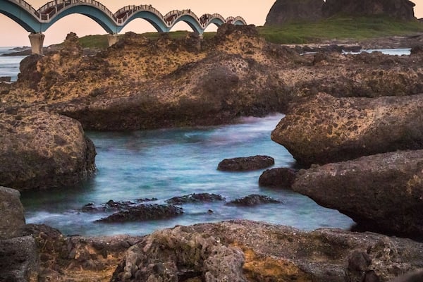 A coastal landscape with a bridge over rocky terrain and calm water.