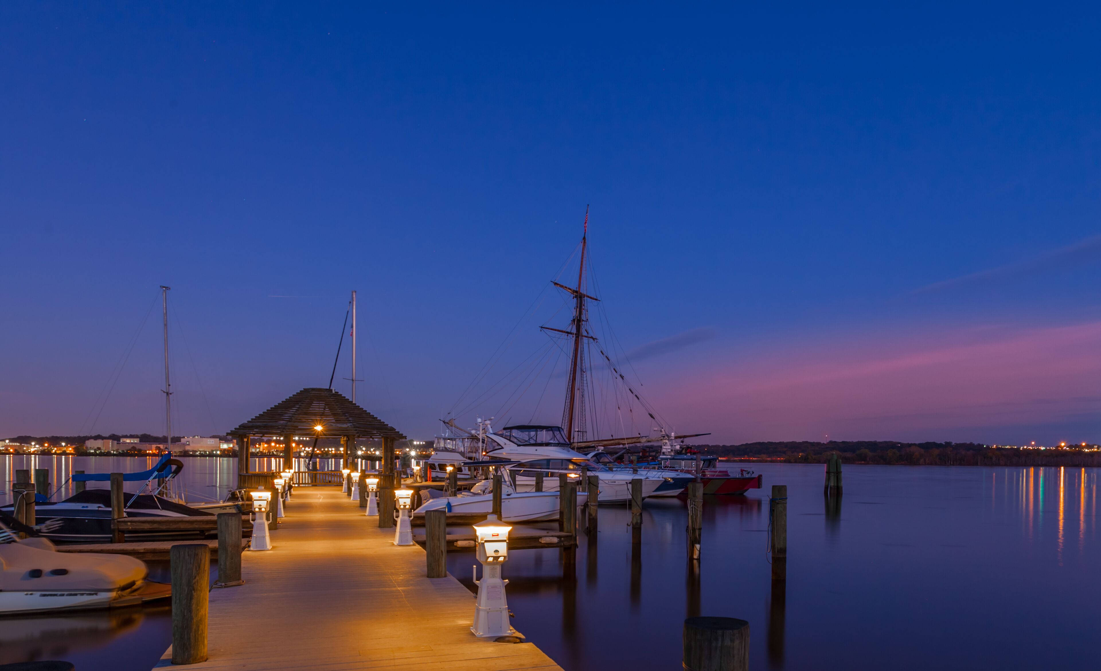 A marina at dusk with boats docked and a wooden pier leading to a covered area.