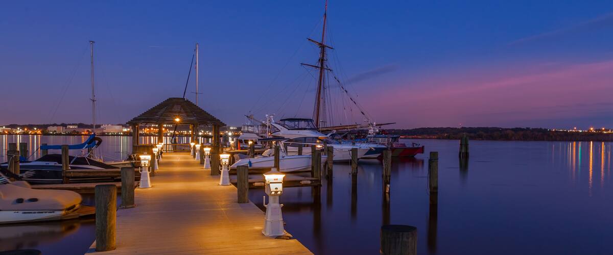 A marina at dusk with boats docked and a wooden pier leading to a covered area.
