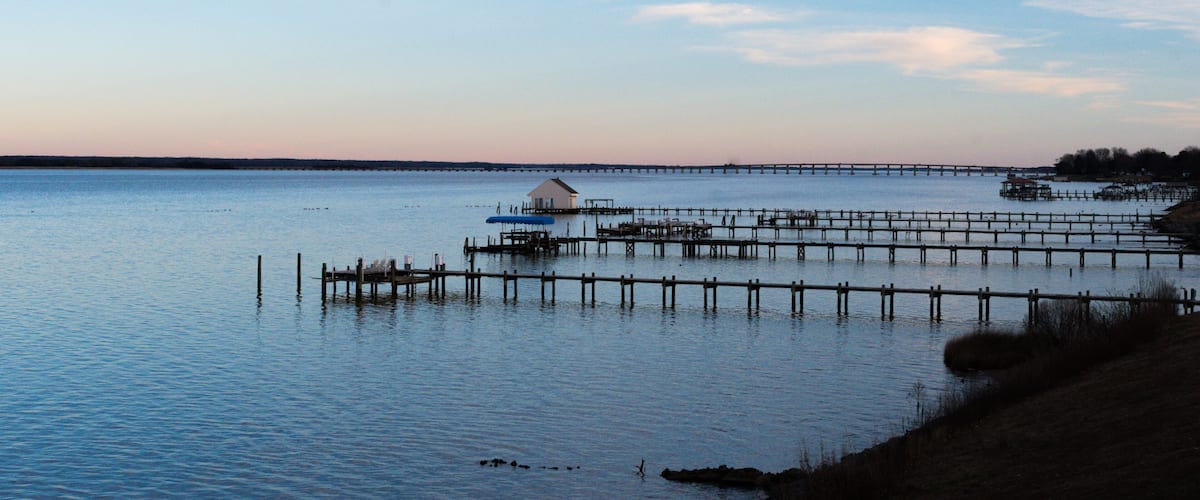 A calm lake with a pier extending into the water, surrounded by a grassy shoreline.
