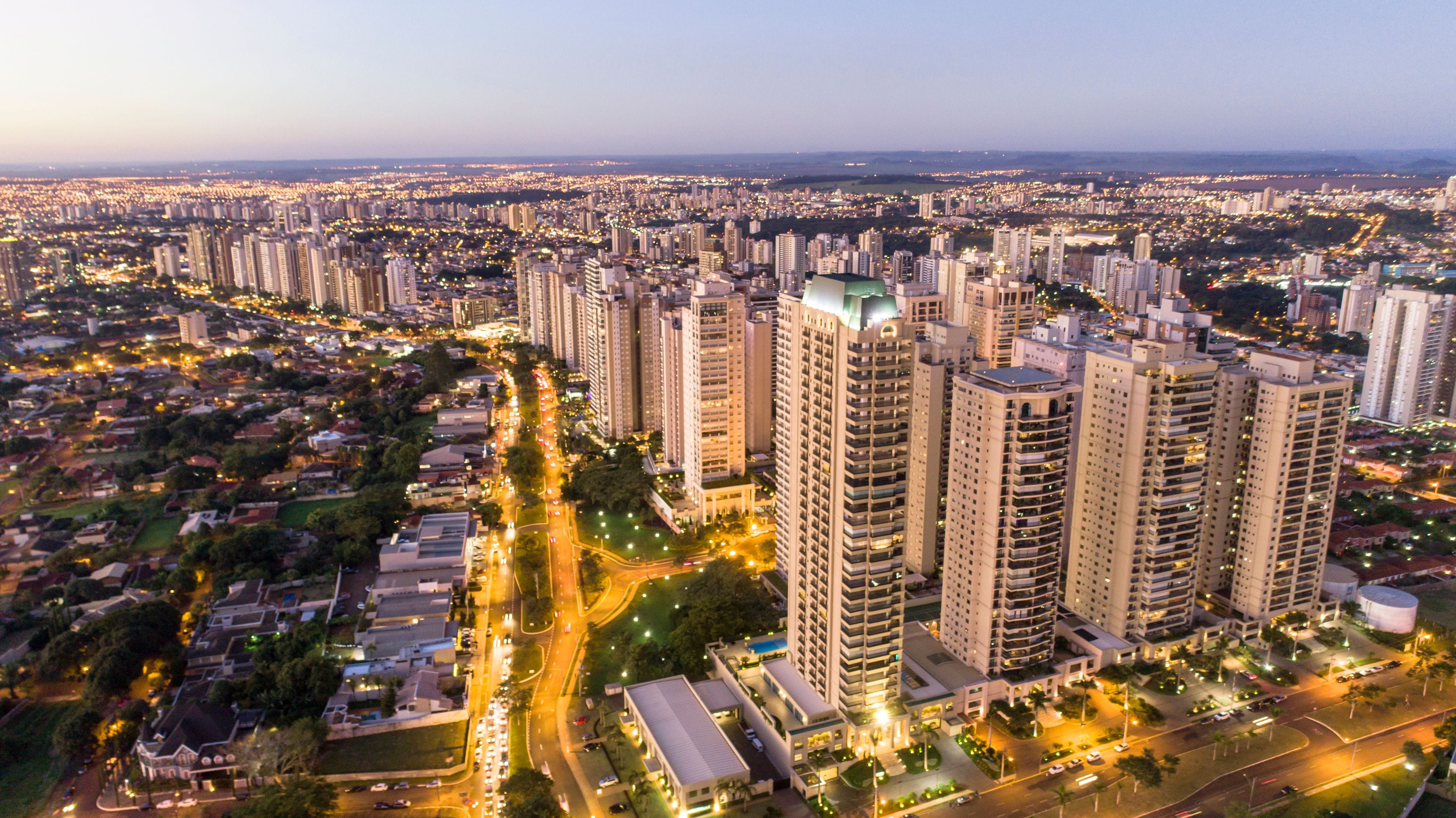 A cityscape at dusk with high-rise buildings, a river, and a dense network of roads.