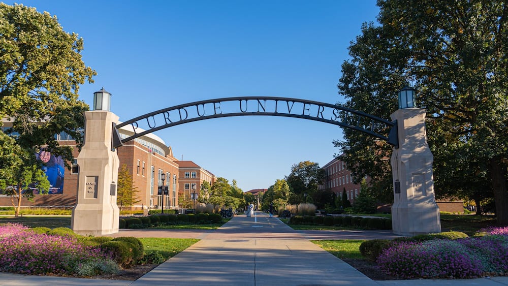 A university entrance archway with the name "PURDUE UNIVERSITY" and a pathway leading to the buildings.