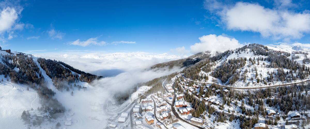 A snow-covered mountain village with a winding road and dense forests.