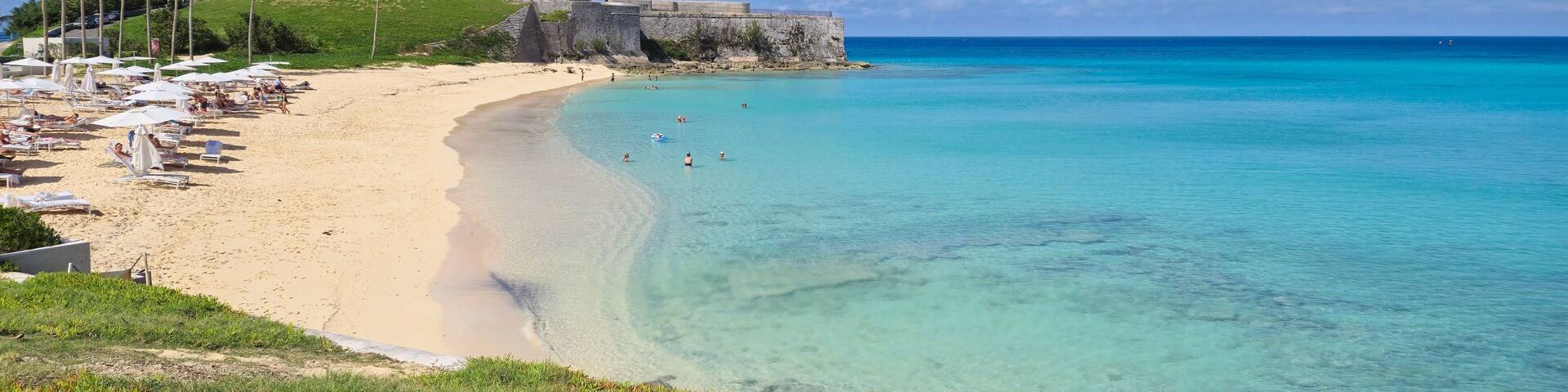 Scenic Bermuda beach with turquoise waters and historic fort.