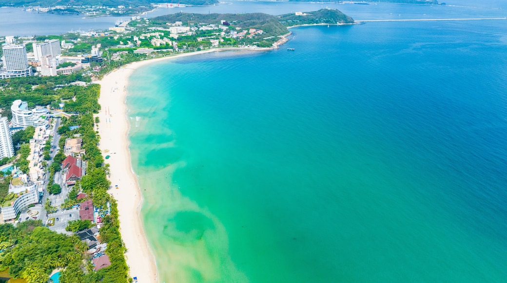 A coastal city with a long sandy beach, clear turquoise waters, and a backdrop of green hills.