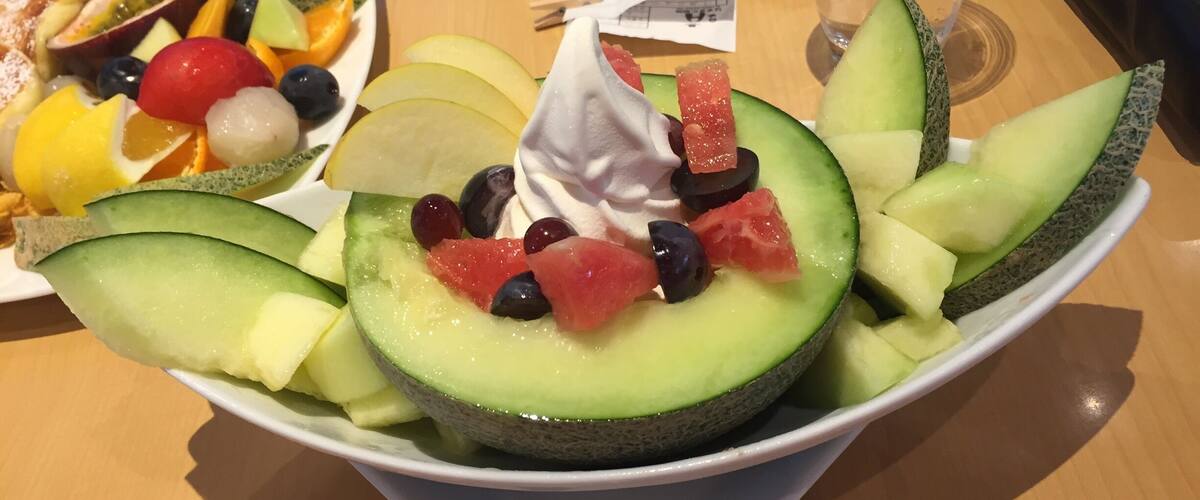 A bowl of melon salad with various fruits and a dollop of cream.