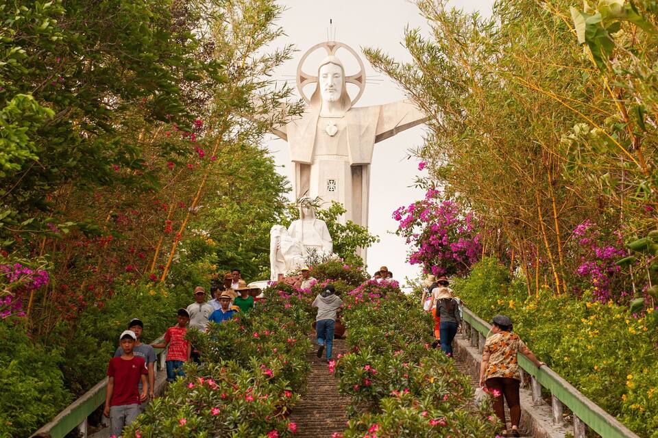A statue at the top of a staircase surrounded by lush greenery and pink flowers.
