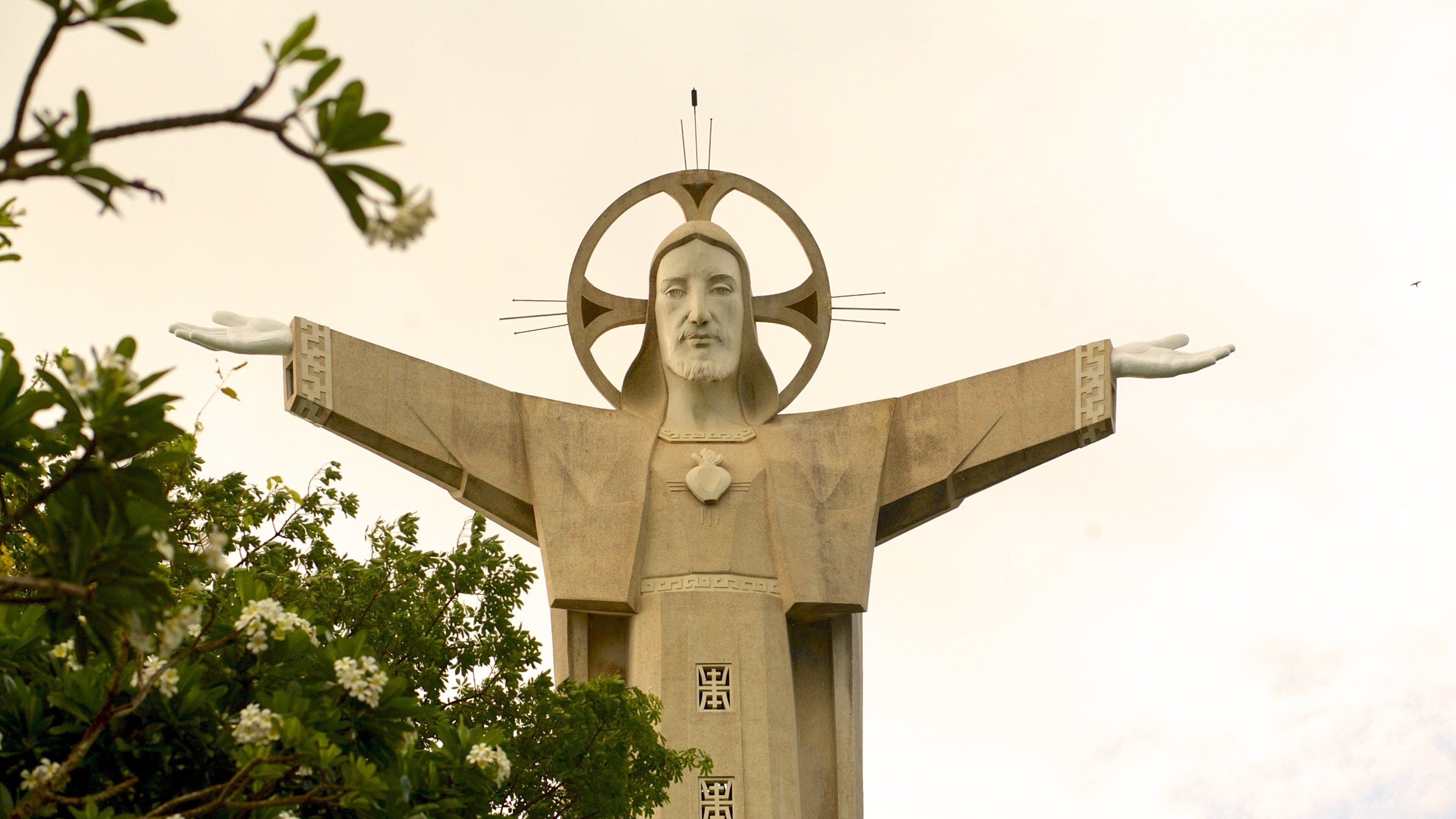 Uma grande estátua com braços estendidos e um halo circular, rodeada por vegetação.
