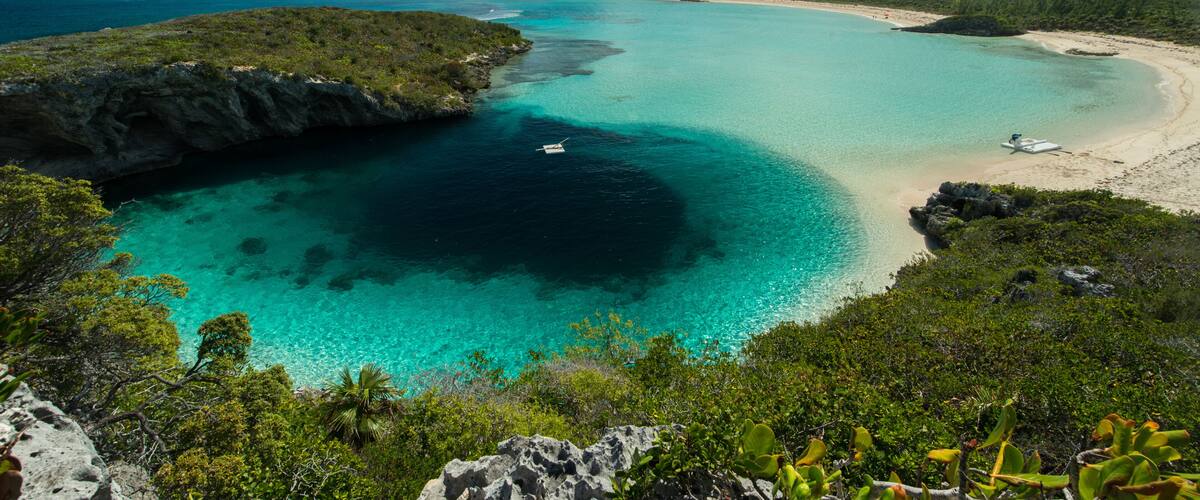 A coastal landscape with clear turquoise waters, a sandy beach, and lush greenery.