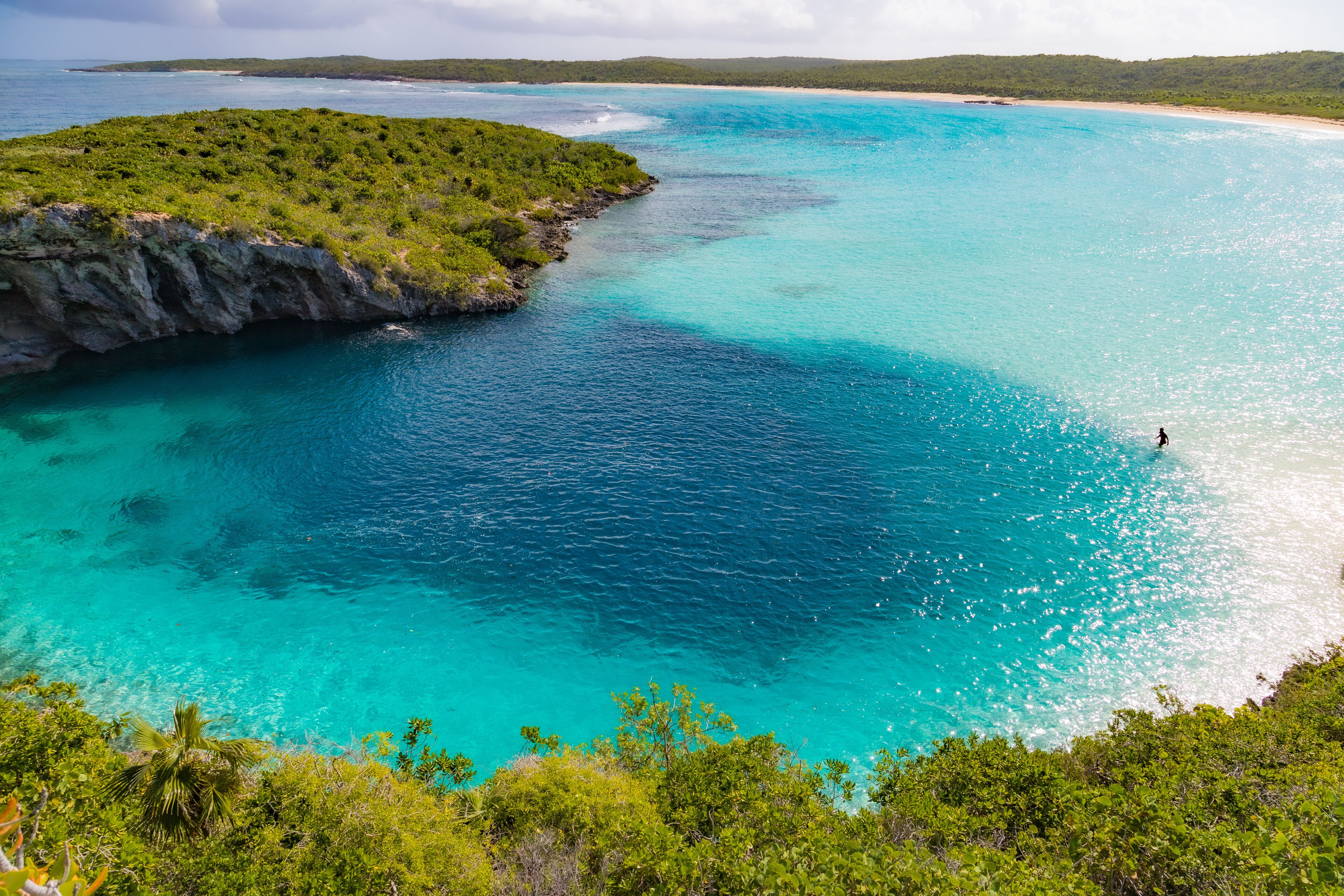 Un paisaje costero con aguas turquesas cristalinas, una playa de arena y abundante vegetación.