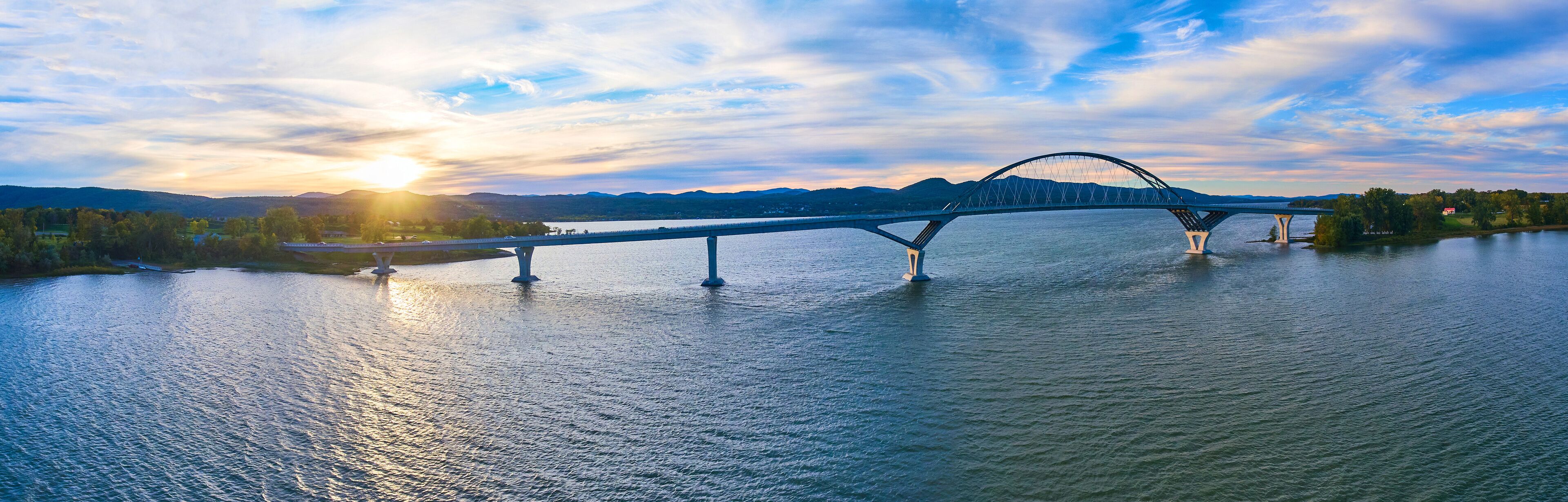 A bridge over a river with mountains in the background and the sun setting.