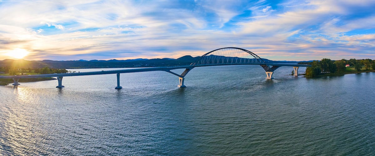 A bridge over a river with mountains in the background and the sun setting.