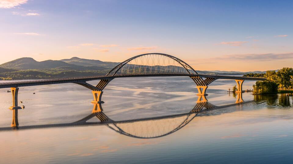 A bridge over a calm river with mountains in the background.