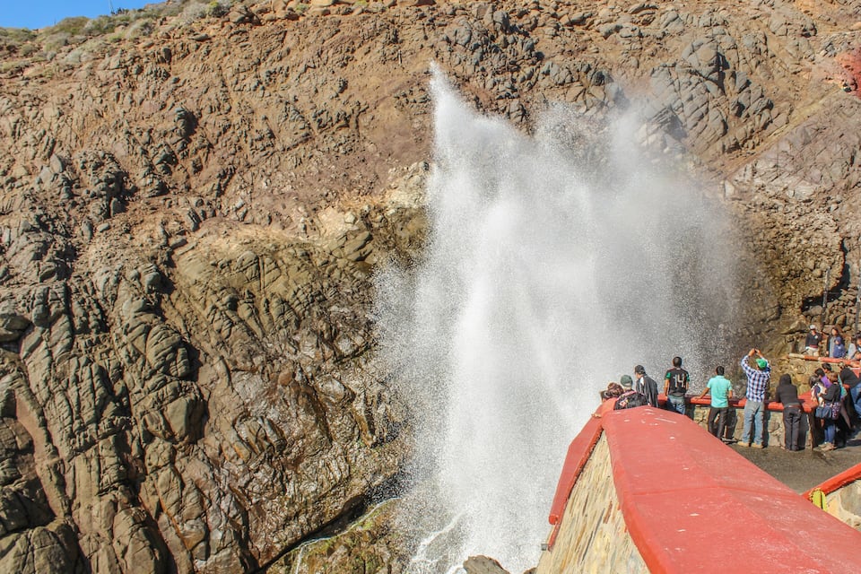 A rocky landscape with a waterfall and a group of people observing it.