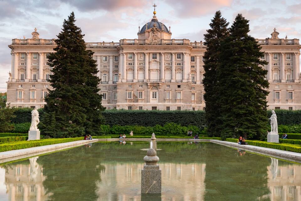 Un magnifique palais à la façade symétrique, doté de grandes fenêtres et surmonté d’un dôme central. Devant, on trouve un jardin magnifiquement entretenu, avec un bassin et des statues.