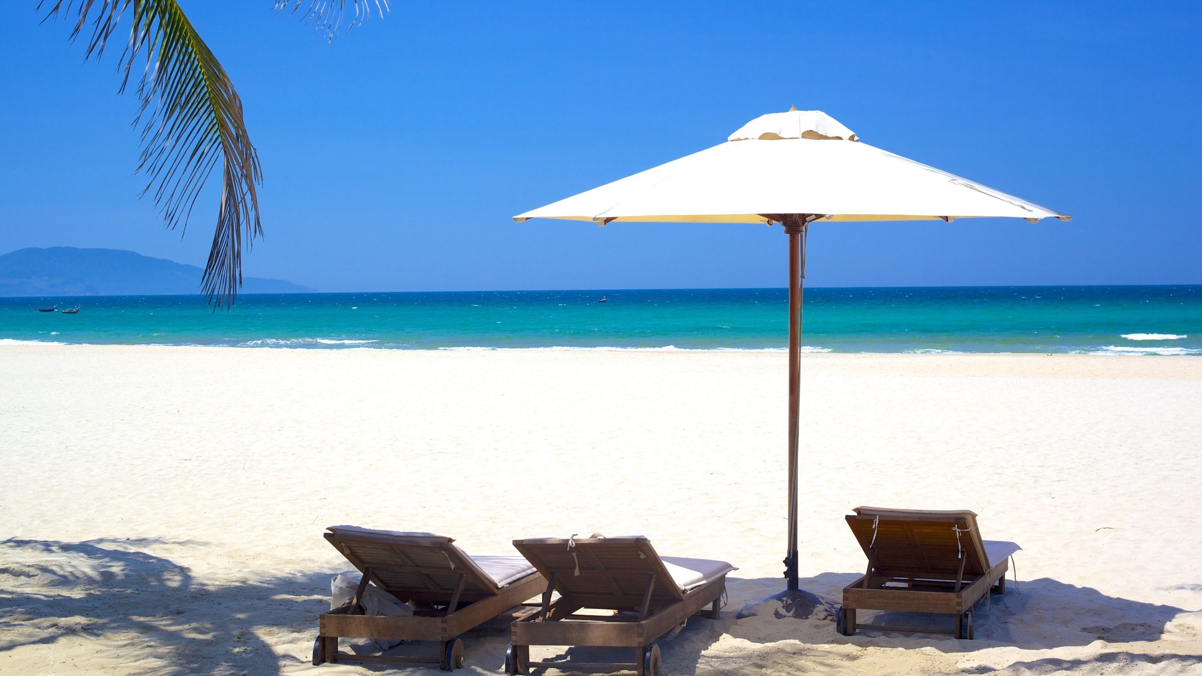A beach with two wooden sun loungers and a white umbrella.